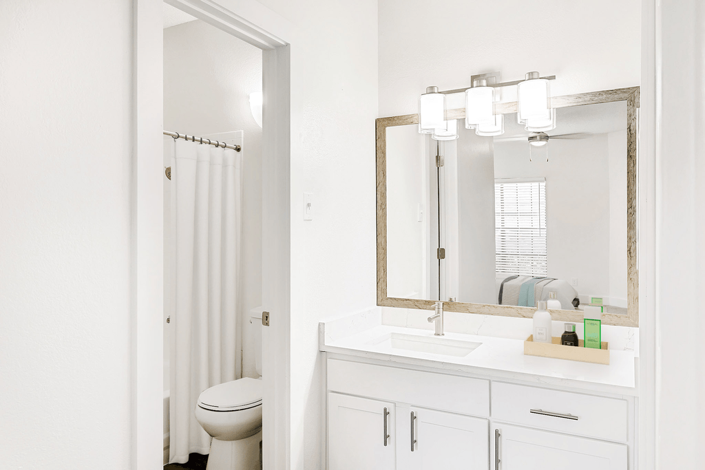 Virtually staged bathroom with white quartz countertop, large mirror, separate door to toilet and tub with white shower curtain